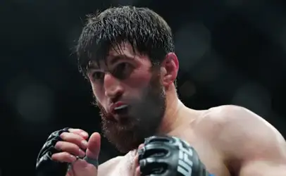 Close-up of a bearded MMA fighter in gloves, sweat on his face, ready to strike in the octagon.