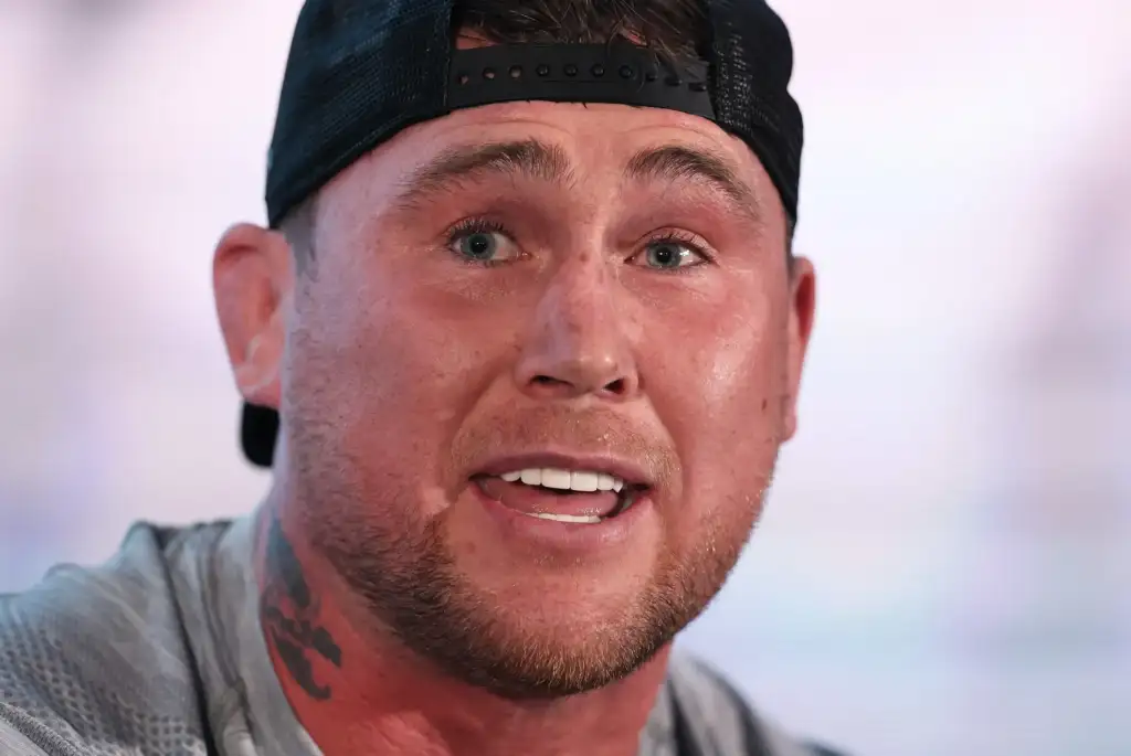 Close-up of a man wearing a backward baseball cap, smiling with visible teeth and blue eyes.