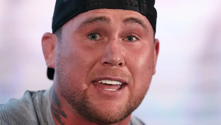 Close-up of a man wearing a backward baseball cap, smiling with visible teeth and blue eyes.