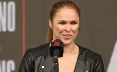 Woman in a black leather jacket speaks at a microphone on a stage during an event