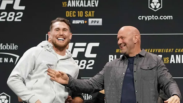 Two men on a stage at a UFC event, smiling and posing, with UFC 282 signage in the background.