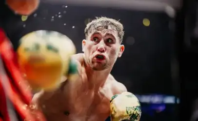 Close-up of a shirtless male boxer with yellow gloves in a match, looking up with a focused, surprised expression.