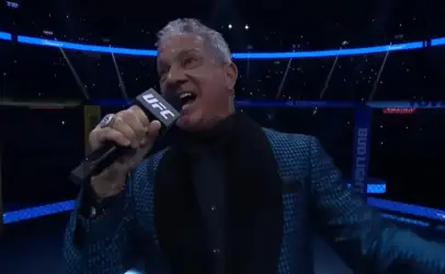 UFC announcer speaking into a UFC-branded microphone inside the octagon, wearing a blue patterned blazer.