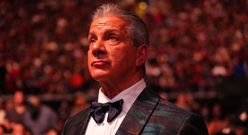 Man in a patterned tuxedo and bow tie gazing upward at a gala, blurred audience in background