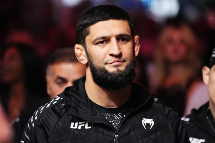 Bearded man wearing a black UFC jacket at a crowded event, looking ahead with a neutral expression.