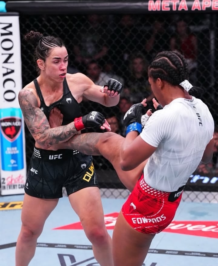 Female UFC fighters in a clinch; one lands a kick to the other’s midsection inside the cage.