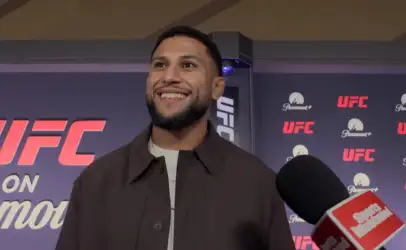 Smiling man with a beard in a dark brown jacket is being interviewed at a UFC event, with UFC and Paramount+ logos in the backdrop.