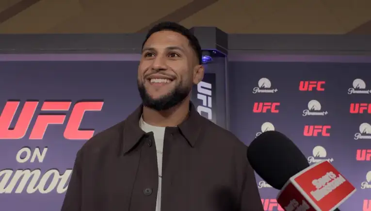 Smiling man with a beard in a dark brown jacket is being interviewed at a UFC event, with UFC and Paramount+ logos in the backdrop.