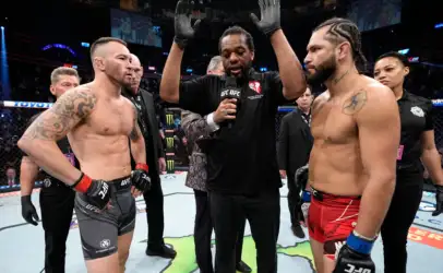 Two muscular UFC fighters face off in the octagon as the referee raises his arms to start the staredown.