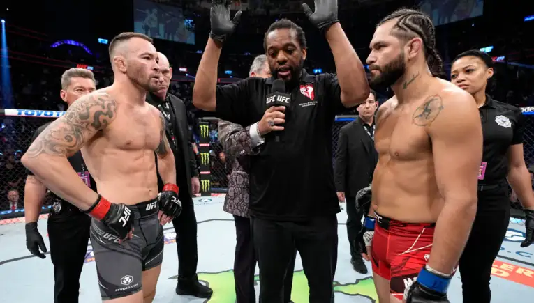 Two muscular UFC fighters face off in the octagon as the referee raises his arms to start the staredown.