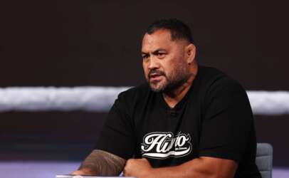 Man with short hair and a beard, wearing a black T-shirt, speaks during an interview in a studio setting