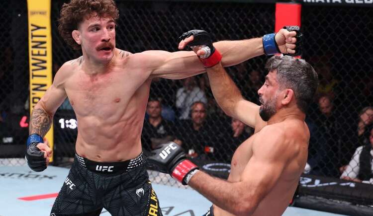 Two UFC fighters exchange punches in the octagon; the left fighter throws a straight, while the right blocks with an arm raised behind his head, crowd watching in the background.