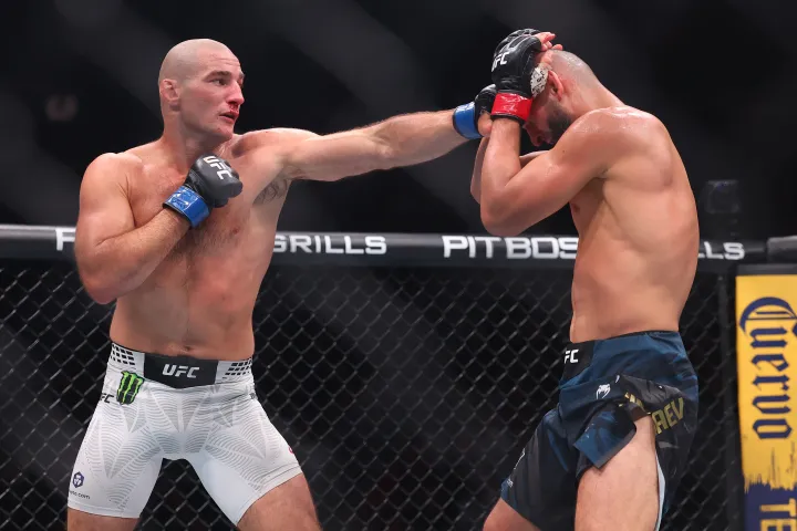 Two UFC fighters clash in the cage as one lands a punch to his opponent's head while the other guards with raised gloves.