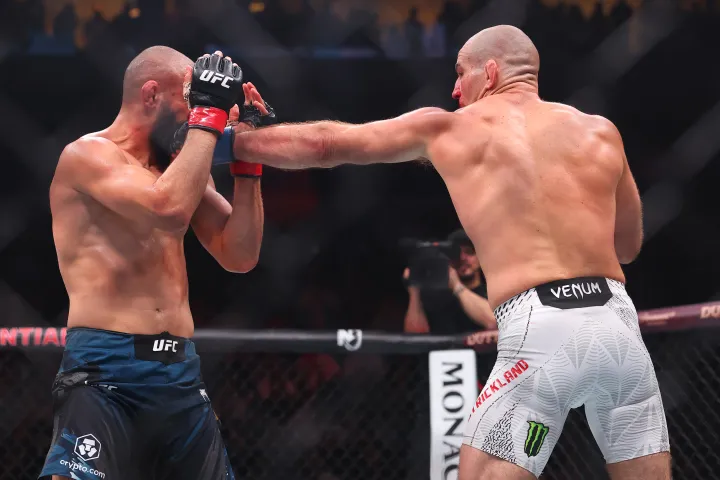 Two bald UFC fighters exchange punches inside the octagon during a match, the punch landing toward the other's face.