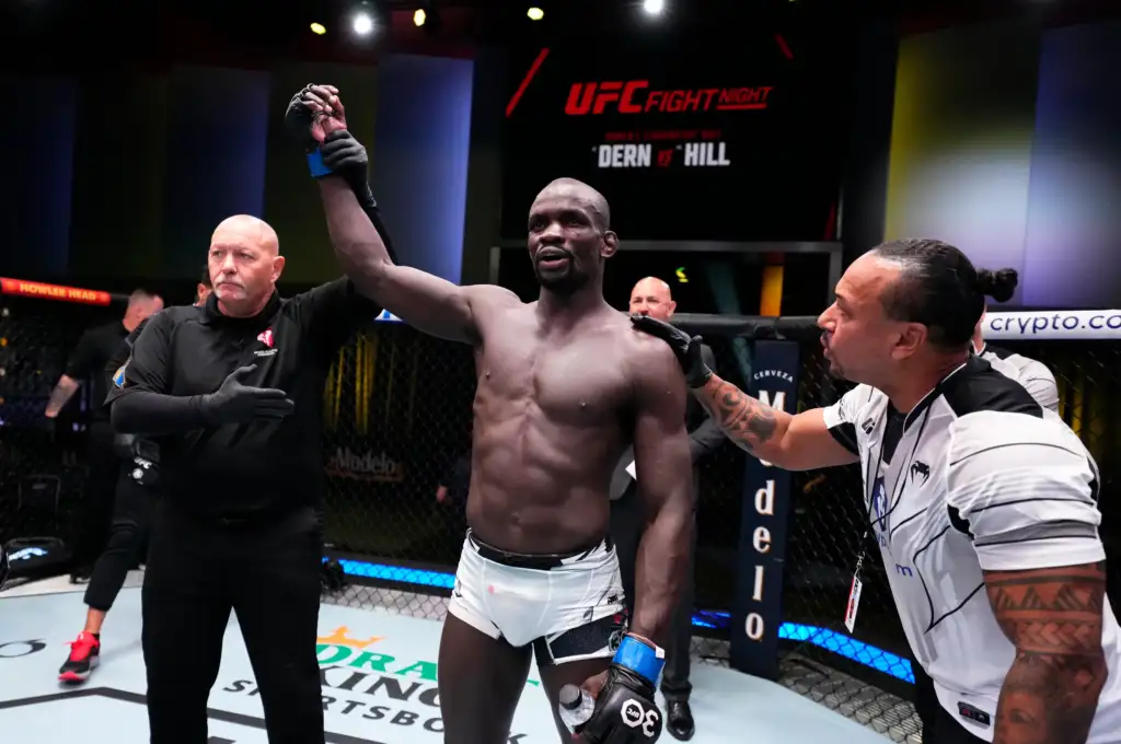 Mma fighter with raised arm, referee declares him winner inside the cage at UFC Fight Night event.