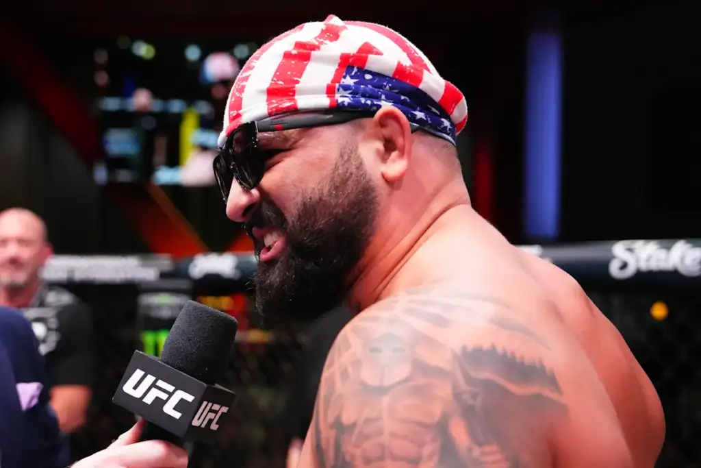 UFC fighter in a star-spangled bandana and sunglasses talks into a microphone inside the cage.