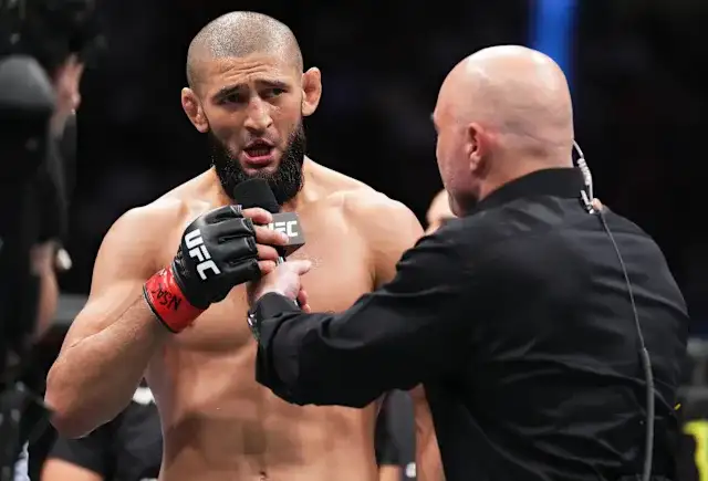 UFC fighter with a beard speaks into a microphone held by a presenter in a black shirt during a post-fight interview.