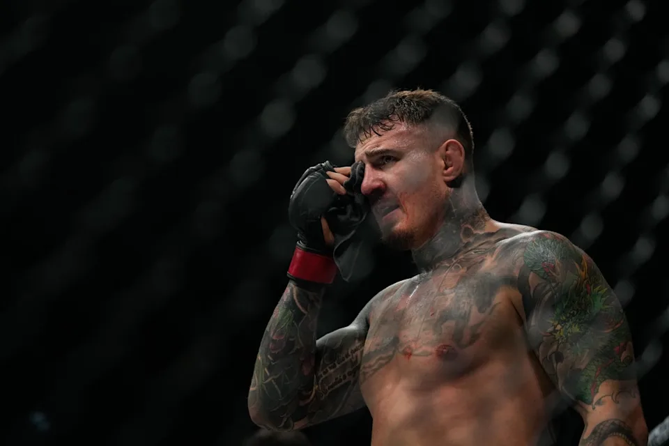 Tattooed male MMA fighter wipes sweat from his face with a cloth inside the cage.