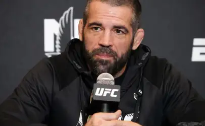 MMA fighter at a UFC press conference, speaking into a UFC-branded microphone, wearing a black hoodie.