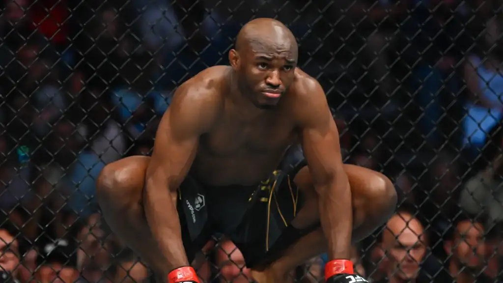 MMA fighter crouching inside a steel cage, wearing black shorts and red gloves, focused and ready to fight.