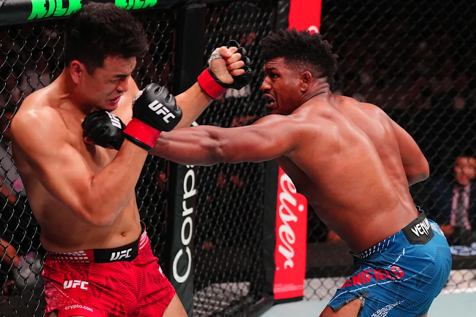 Two shirtless UFC fighters clash in the cage as one lands a punch on the other's guard.