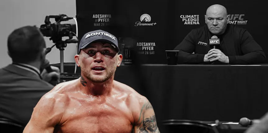 Shirtless MMA fighter wearing a cap, sweating, facing the camera at a press conference with a cameraman and a questioning figure in the background.
