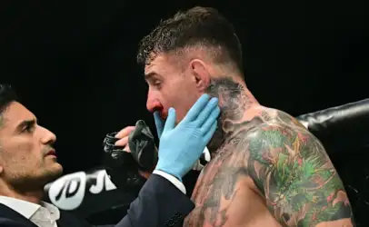 Boxer with colorful tattoos receives care from a trainer wearing blue gloves in a boxing ring corner.