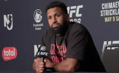 UFC fighter with a beard sitting at a press conference, holding a microphone.