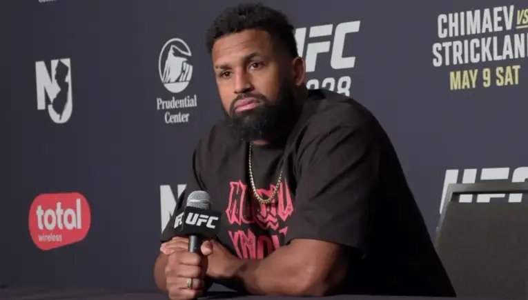 UFC fighter with a beard sitting at a press conference, holding a microphone.