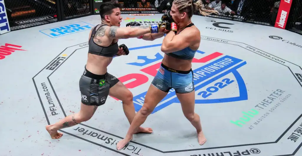 Two female mixed martial artists exchange punches inside an arena cage during a championship bout, centered on a mid‑ring exchange with the crowd watching above.