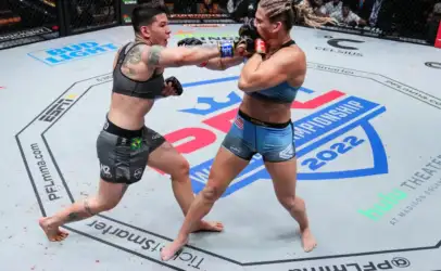 Two female mixed martial artists exchange punches inside an arena cage during a championship bout, centered on a mid‑ring exchange with the crowd watching above.