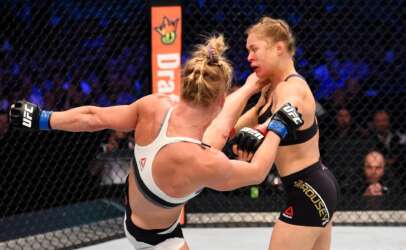 Two female UFC fighters in the octagon trading blows, one in a white top and the other in black shorts.