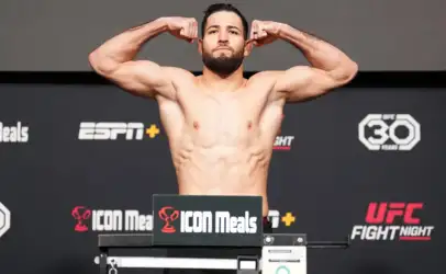 Male shirtless MMA fighter flexing on the weigh-in stage, arms raised, in front of branded backdrop (UFC, ICON Meals)