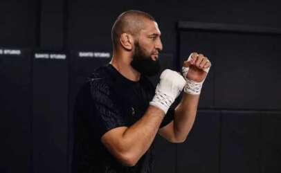 Bearded man in a black shirt practicing boxing with white hand wraps in a gym.