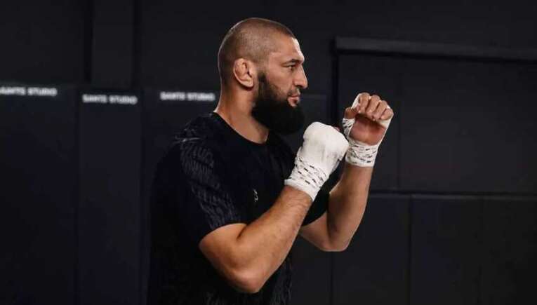 Bearded man in a black shirt practicing boxing with white hand wraps in a gym.