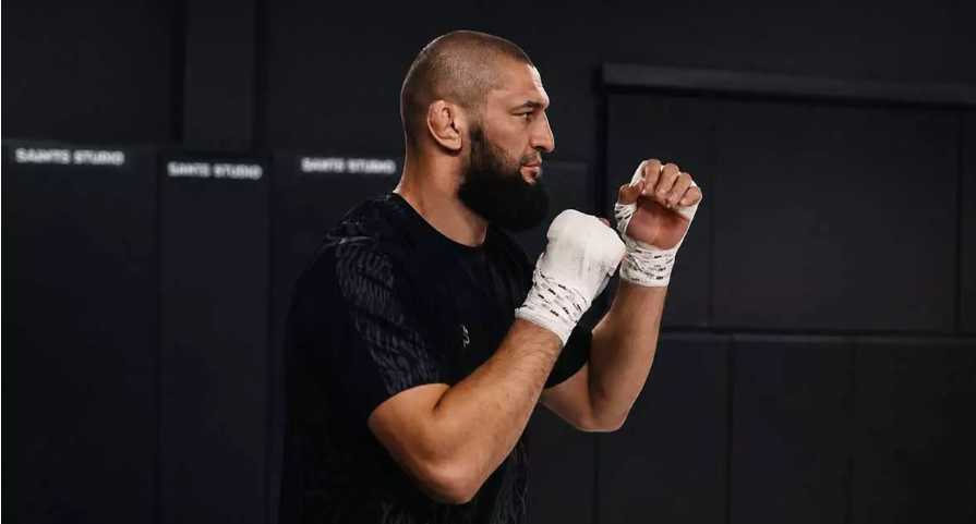 Bearded man in a black shirt practicing boxing with white hand wraps in a gym.