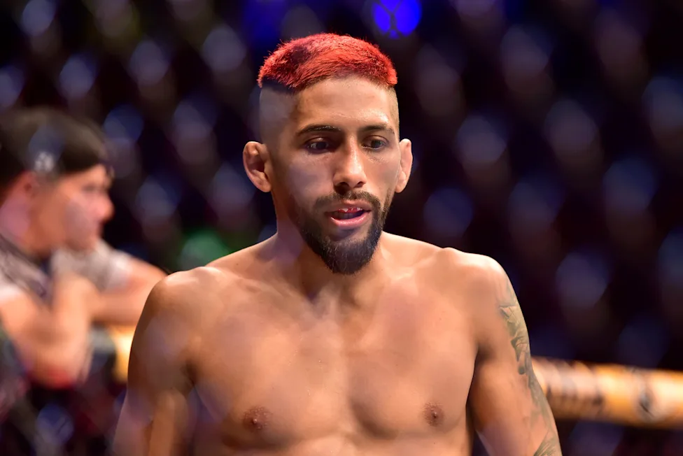 Male fighter, shirtless with red hair and beard, in a combat sports ring, looking to the side.