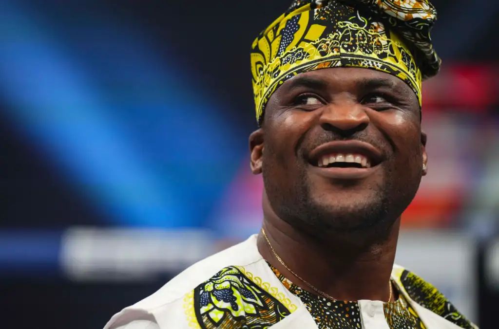 Close-up of a smiling man wearing a vibrant yellow and black patterned headwrap and matching outfit.