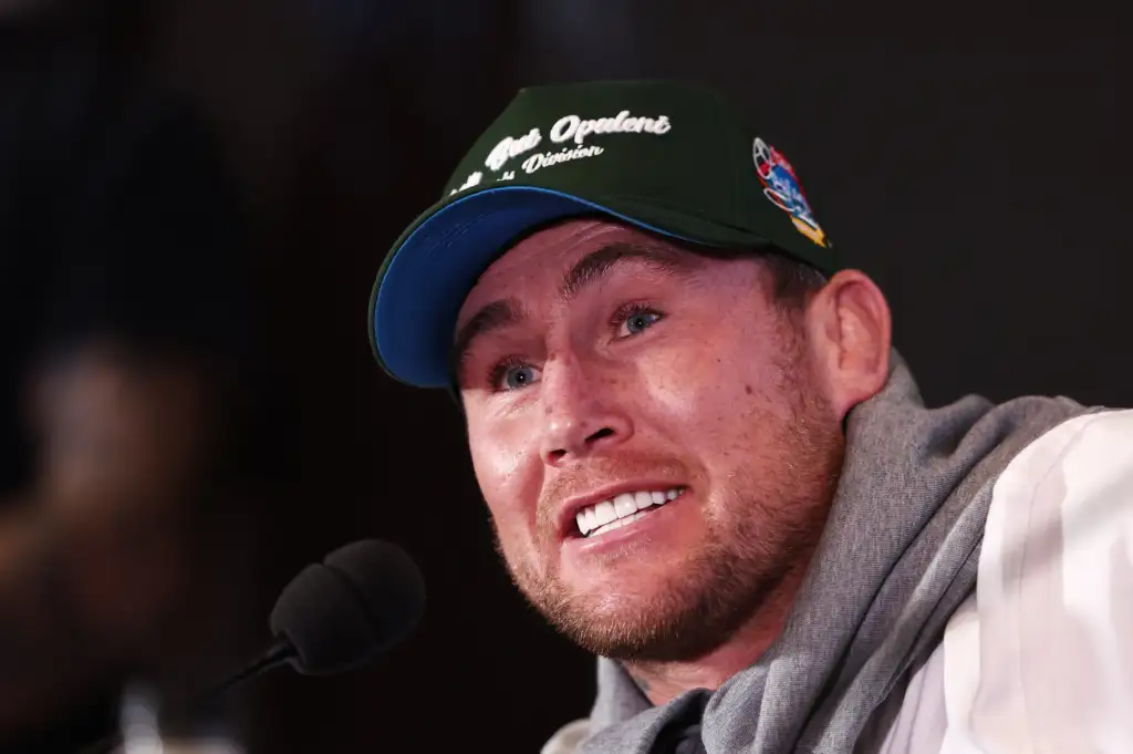 Man wearing a green cap with a blue brim, smiling while speaking into a headset microphone.