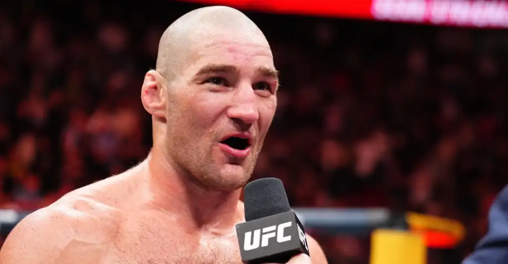 Close-up of a bald, muscular UFC fighter speaking into a microphone during a post-fight interview.
