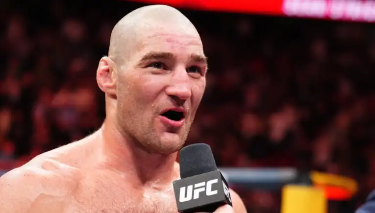 Close-up of a bald, muscular UFC fighter speaking into a microphone during a post-fight interview.
