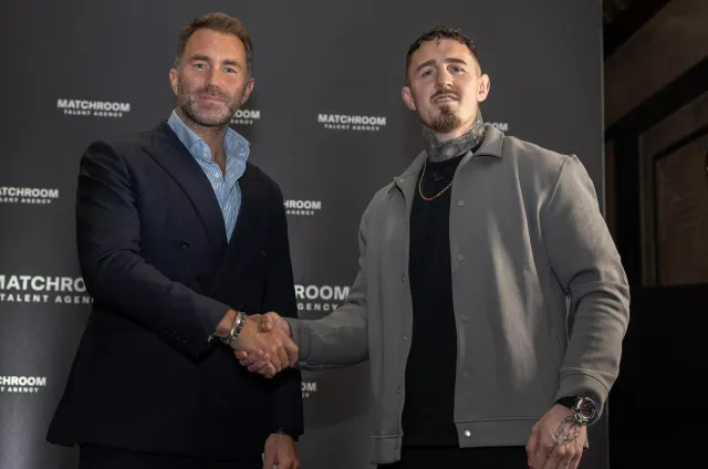 Two men shake hands in front of a black backdrop with Matchroom logos, dressed in smart-casual suits at a formal event.
