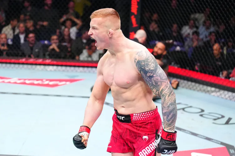 MMA fighter in red shorts and black gloves, shouting with arm raised inside a cage during a match