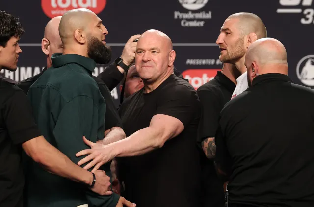 Group of muscular men on a stage at a weigh-in, some grabbing each other’s arms in a tense face-off before a boxing/MMA event.
