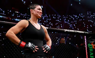 Female mixed martial artist stands in the cage, wearing a black outfit and red gloves, looking toward the crowd with a smile.
