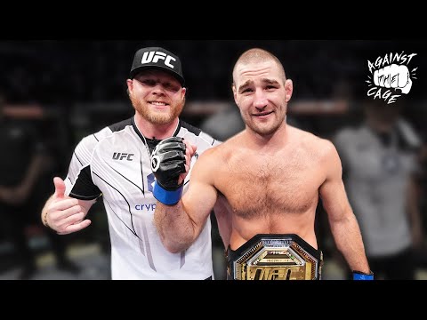 Two UFC fighters pose in the octagon after a fight; one is shirtless wearing a championship belt, both giving thumbs up in celebration.