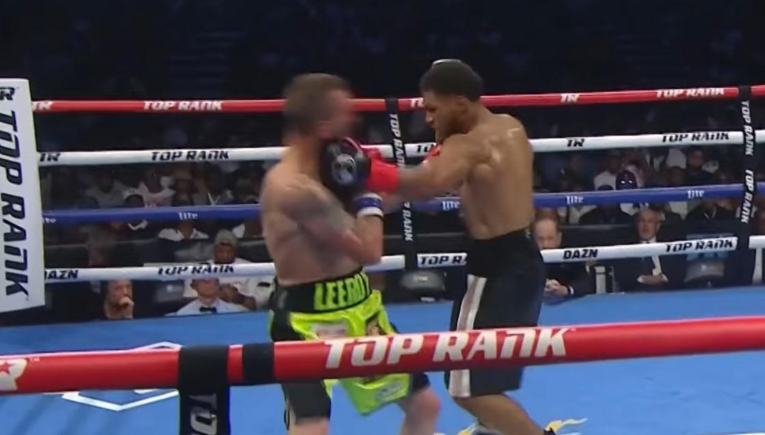 Two shirtless boxers trade punches inside a ring with red, white, and blue ropes marked 'TOP RANK' and 'DAZN' in the background.