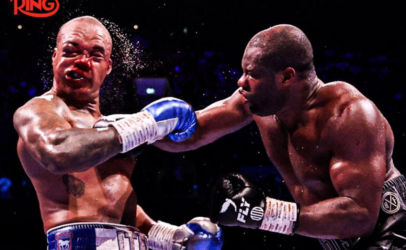 Two muscular boxers exchange punches mid-match, one wearing blue gloves with Ring logo visible in the corner.