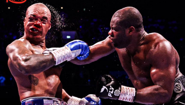 Two muscular boxers exchange punches mid-match, one wearing blue gloves with Ring logo visible in the corner.