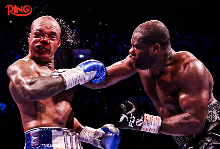 Two boxers in a ring exchange punches; the left fighter lands a punch on the right fighter's face, Ring logo visible in the corner.